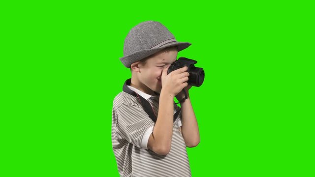 Little boy photographer in hat takes photo at green background