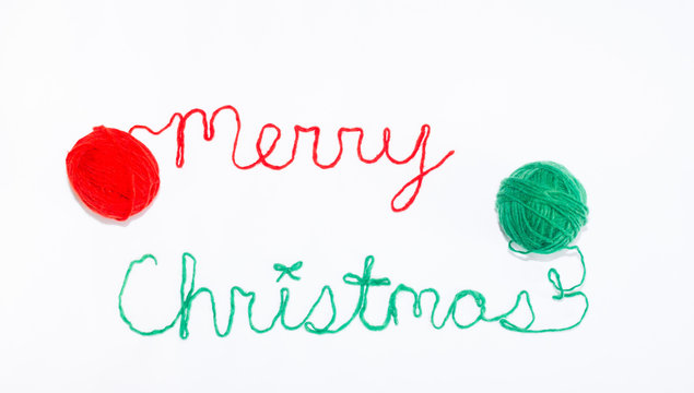 Merry Christmas Written in red and green Yarn with Balls of Yarn on Each Side. Photographed against a white background. 