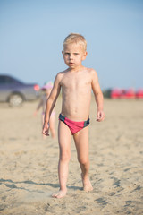 Baby boy walking on the sandy beach near the sea. Cute little kid at sand tropical beach. Ocean coast.