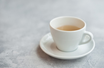 Morning photo, breakfast on a light concrete background. White cup on white saucer with tea.
