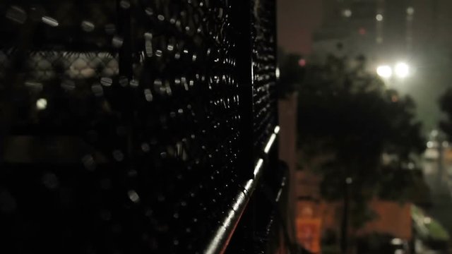 Night rain in Bangkok. View on wet street from balcony through rabitz net. Thailand.