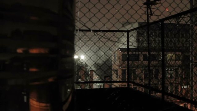 Night rain in Bangkok. View on wet street from balcony through rabitz net. Thailand.