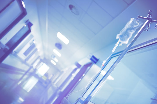 Blurred hospital corridor with a drip system on the pole, unfocused background.