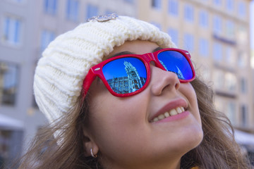 Sights of the old city are reflected in the glasses on the face of a young smiling girl, close-up, Munich, Germany