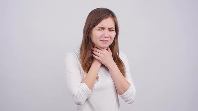 A young woman has a sore throat on a gray background