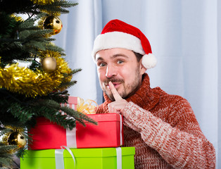 man wearing Santa puts gifts under the Christmas tree