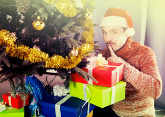man wearing Santa puts gifts under the Christmas tree