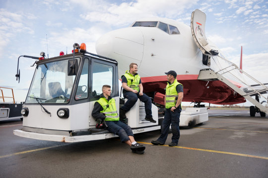 Workers Sitting On Tow Truck While Friend Standing Against Airpl