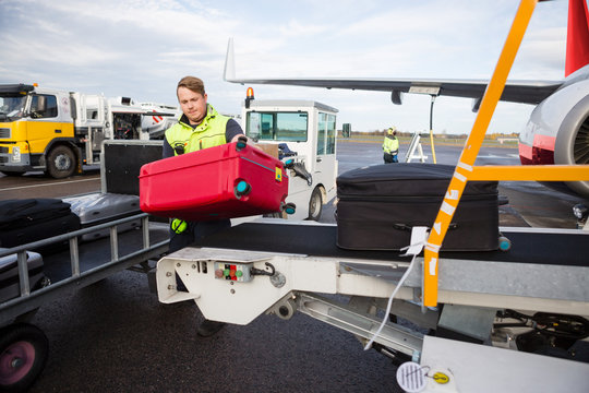 Worker Unloading Luggage From Conveyor Attached To Airplane