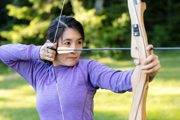 Confident Woman Aiming With Bow And Arrow In Forest