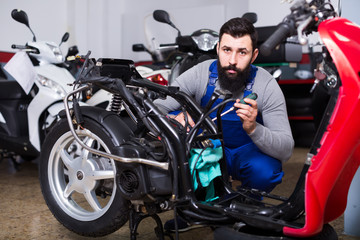 Young male worker working at restoring motorbike in workshop