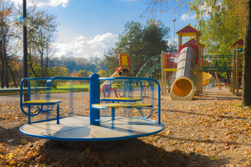 Children playground consisting of rotating carousel, swing, tube and climbing frame. Fallen autumn...
