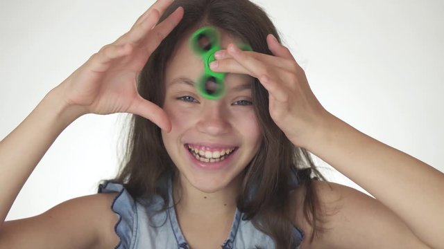 Beautiful cheerful teen girl spinning a green fidget spinner on her forehead on white background stock footage video