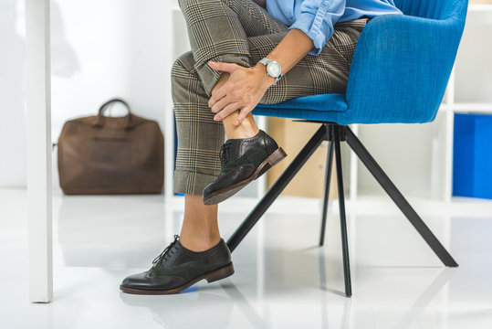 Cropped View Of Tired Businesswoman With Painful Legs Sitting In Chair