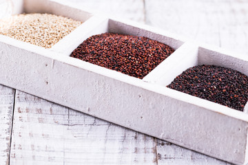 Red, black and white quinoa seeds on a wooden background