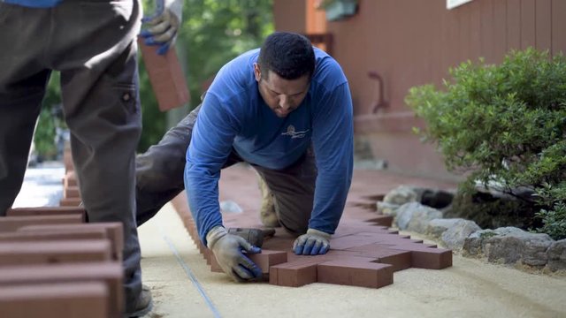 Using a rubber mallet, a hardscaper taps the red brick pavers into place.