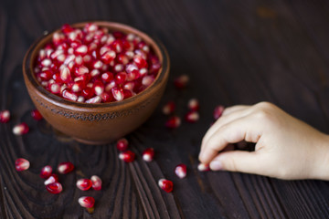 ruby pomegranate seeds in a bowl on a wooden table, a hand reaches out to pomegranate seeds