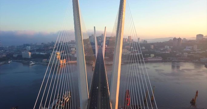 Statatic aerial view of the Zolotoy Bridge (the Golden Bridge, built in 2012) and cars driving across it. It's cable-stayed bridge across the Zolotoy Rog harbour. Vladivostok, Russia. Autumn sunrise
