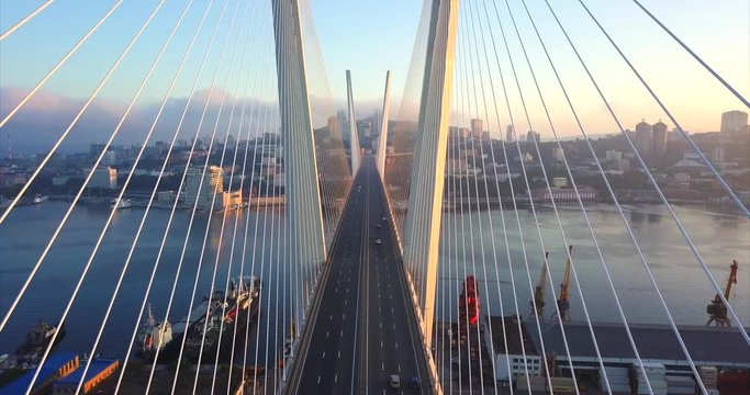 Ascending above the road between stay cables of Zolotoy Bridge (Golden Bridge, cable-stayed bridge across Zolotoy Rog harbour built in 2012). Aerial view of cars driving across it. Vladivostok, Russia