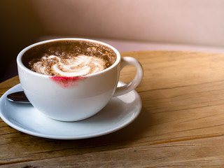 Hot latte with latte art in white coffee cup with red color lipstick stain on wooden table in a morning