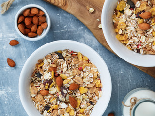 Top view of the breakfast for two person with muesli with almond nuts and dried berries in white bowls and milk on the blue textured table.