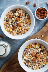 Top view of the breakfast for two person with muesli with almond nuts and dried berries in white bowls and milk on the blue textured table.