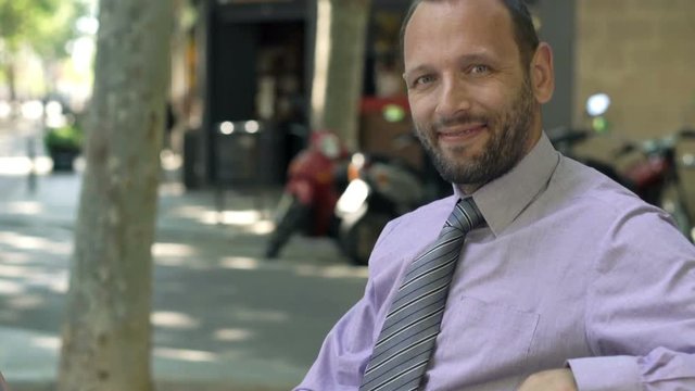 Portrait of happy businessman with laptop sitting on bench in city

