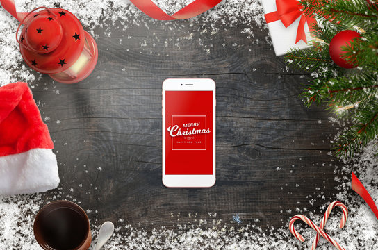 Smart phone surrounded with Christmas decorations. Top view scene. Red isolated screen for mockup.