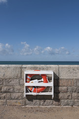 Lifebuoy ring fixed to wall by the sea in foregorund Portrait format
