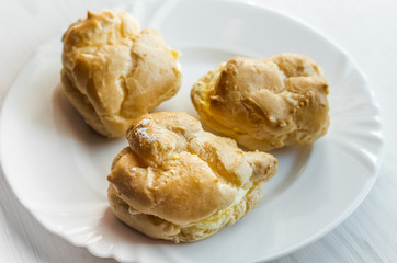 Homemade baked cream puffs on the white plate on light wooden table