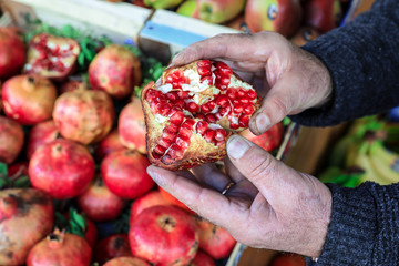 Half of the ripe pomegranate fruit on the palms of the seller in the greek vegetable shop.