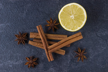 Fototapeta na wymiar Cinnamon sticks, lemon and anise stars on a black stone background.