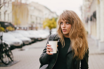Portrait of a beautiful girl on a city street, holding a paper cup in her hand