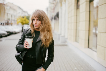 Portrait of a beautiful blonde girl on a city street, holding a paper cup in her hand