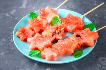 Watermelon in the form of stars on skewers with leaves of mint lies on a plate. The blue dish is like a rocket in space. Top view.