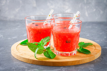Watermelon smoothies in glasses with mint leaves on a gray dark concrete background.