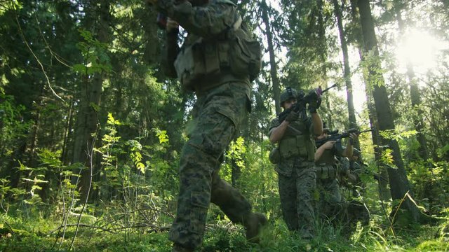 Squad of Five Fully Equipped Soldiers in Camouflage on a Reconnaissance Military Mission, Aiming Rifles. They're Moving in Formation Through Dense Forest. Low Angle Footage.