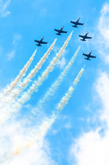 Group of fighter planes fly up with a smoke track against a blue sky with clouds.