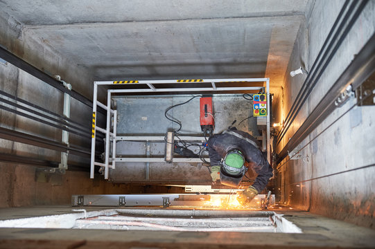 lift worker welding elevator fasteners in lift shaft