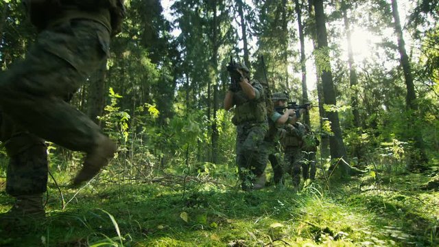 Squad of Five Fully Equipped Soldiers in Camouflage on a Reconnaissance Military Mission, Aiming Rifles. They're Moving in Formation Through Dense Forest. Low Angle Footage.