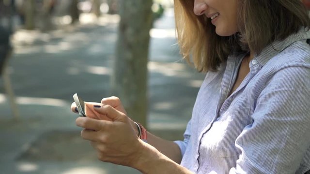 Happy woman playing game on smartphone sitting on bench in city

