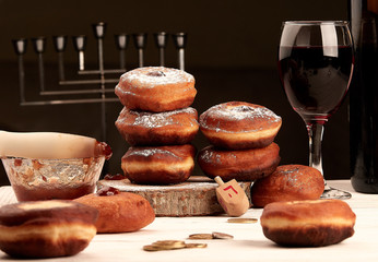 donuts with jam, shell, eggs, wine, dreidel, coins, chanukiah on a white table and black background