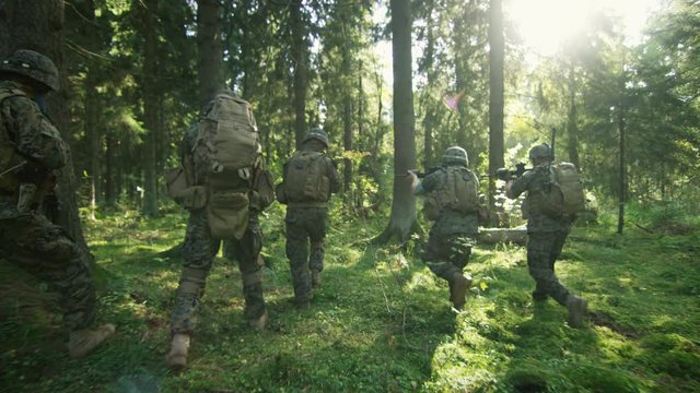 Squad of Five Fully Equipped Soldiers in Camouflage on a Reconnaissance Military Mission, Rifles Ready. They're Moving in Formation Through Dense Forest. Following Back View Shot.