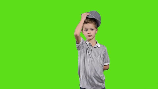 Cute little child take off hat and welcomes at green background