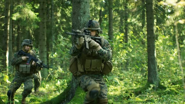 Squad of Five Fully Equipped Soldiers in Camouflage on a Reconnaissance Military Mission, Rifles in Firing Position. They're Moving in Formation Through Dense Forest. 