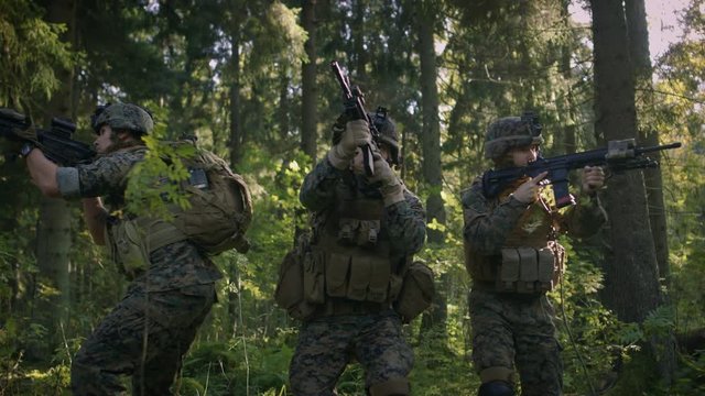 Three Fully Equipped Soldiers Wearing Camouflage Uniform Attacking Enemy, Theyr're in Shooting Ready Stance, Aiming Rifles. Military Operation in Action, Squad Standing in Dense Forest.
