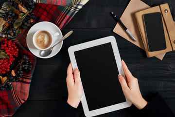 Women hands holding the tablet with black screen above the table with a cup of coffee and smart
