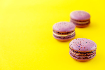 Macaron or macaroon french coockie on yellow background with purple flowers, pastel colors. Flat lay. Food concept.