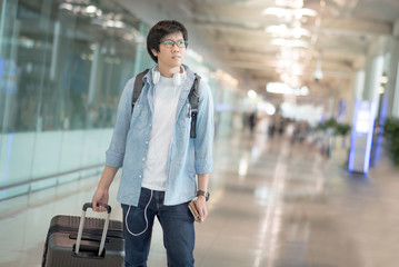 Young Asian man dressed in casual style walking with suitcase luggage in the international airport terminal, travel lifestyle concepts