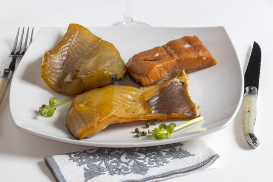 Diff&eacute;rents poissons fum&eacute;s dans une assiette et couvert sur fond blanc